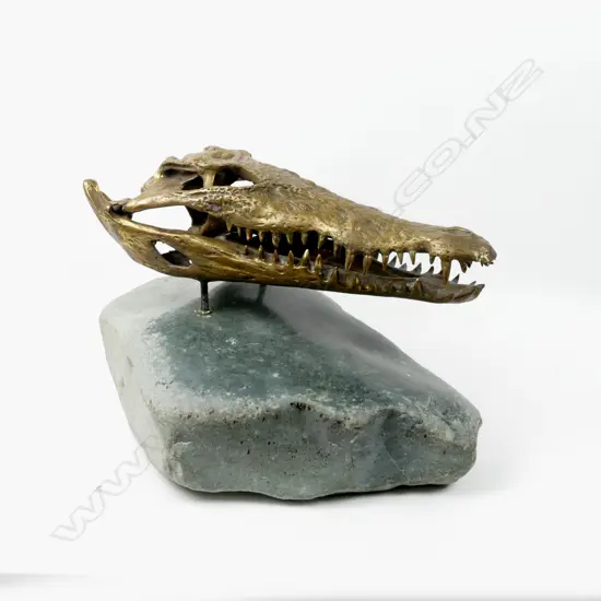 A brass sculpted crocodile skull on a serpentine boulder