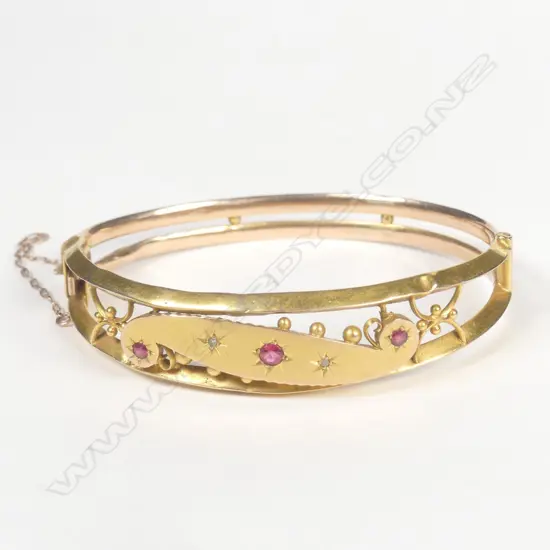 An early 20thC gilded 9ct. rose gold and gem set hinged bangle
