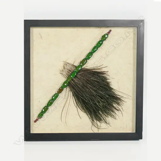 A framed strip of green beetles mounted on stick with brightly coloured feathers,