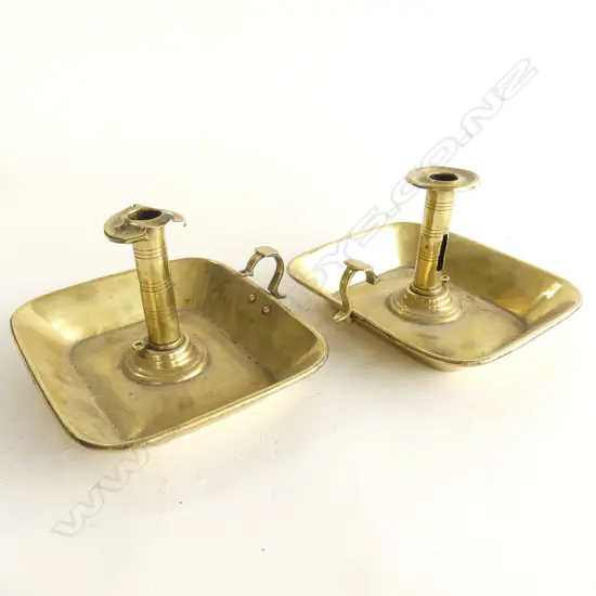 A pair of Victorian brass chambersticks, with wide rectangular drip-tray bases with flared rims, scroll handles, some damage and snuffers absent. .