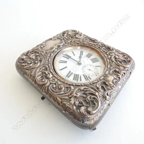 The large watch with Roman numerals to the white enamel dial. Apparently working. The embossed silver cover hallmarked Birmingham 1903 with strut back. 115 x 105mm