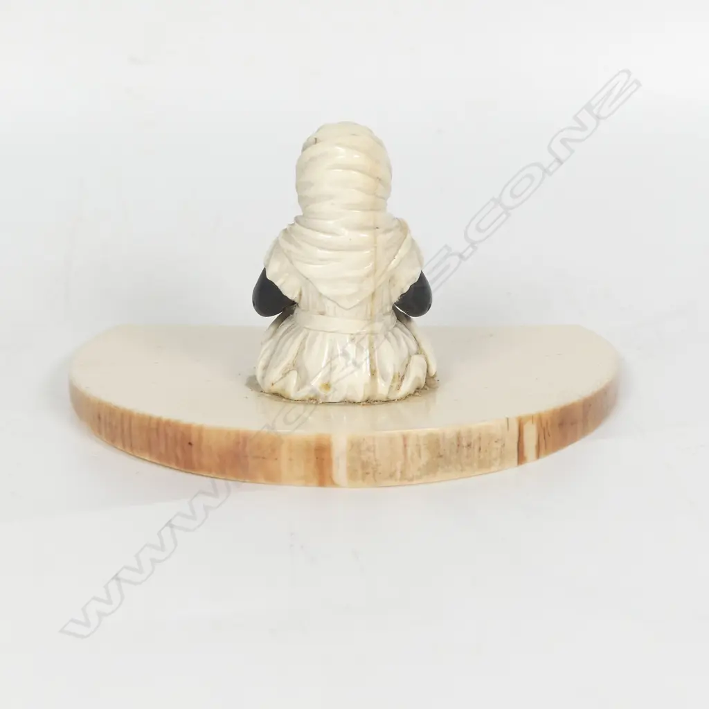 A racially caricaturing carved ivory and ebony figure of a black girl seated with a dinner plate carrying a single large cricket insect Image 1++