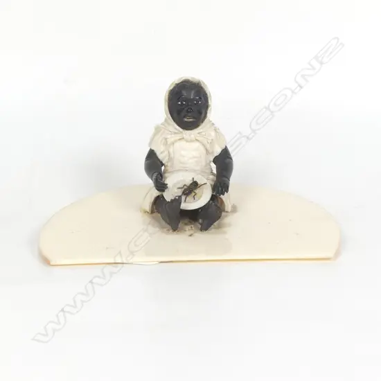 A racially caricaturing carved ivory and ebony figure of a black girl seated with a dinner plate carrying a single large cricket insect