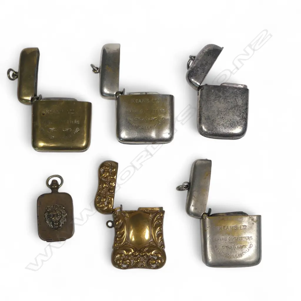 Five silver plate and brass vesta cases (three advertising Kean's Naval Outfitters Wellington & Auckland) and a small pill box with lion's head relief decoration. Image 1++