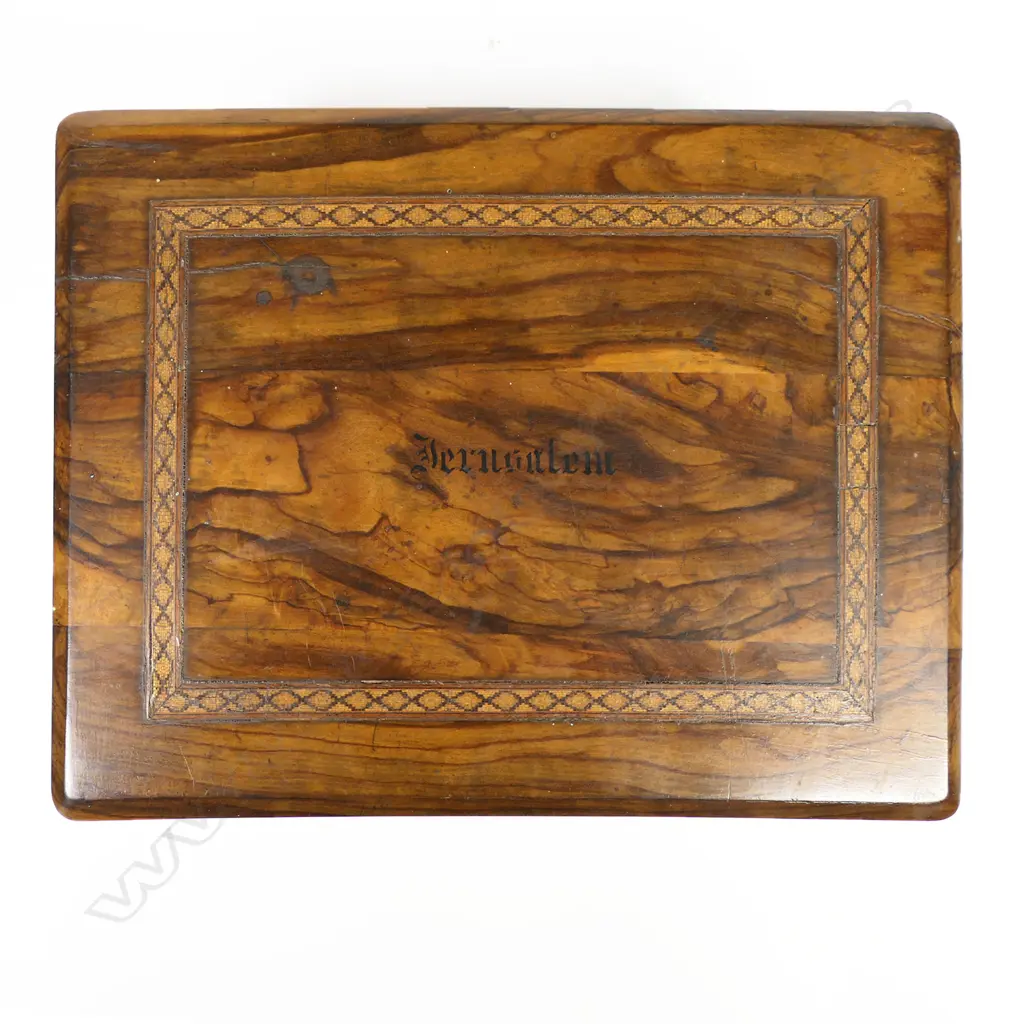 An olive wood work box, souvenir of a pilgrimage to the Middle East, oblong, undecorated except for a band of fine Tunbridge inlay framing the inked name 'Jerusalem'. Interior fitted with a lift out upper tier of small lidded compartments, silk winders and pincushion. 255 x 155 x 110mm Image 1++