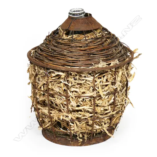 An old glass wine flagon in steel cage with moss & straw padding,