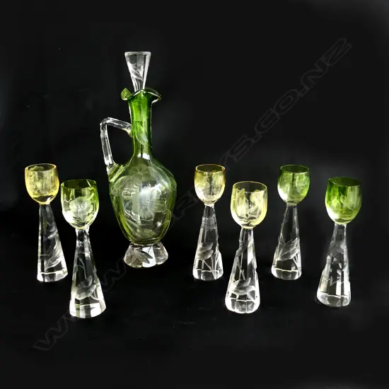 A Moser decanter & 5 glasses (1 w staple repair) c.1910. The decanter with green body and clear handle and faceted base. Intaglio cut with florals. H.300mm. The conforming glasses include three green and two amber toned. H.160mm. one repaired. Note: Moser is a world recognised luxury glass manufacturer based in Karlovy Vary
