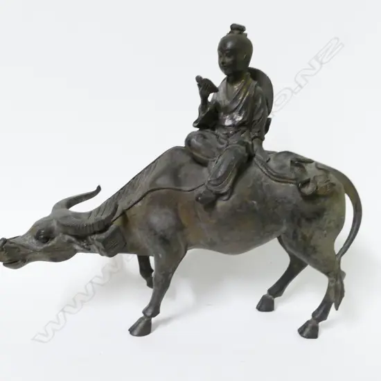 A Chinese cast metal statuette of a young boy seated on the back of a water buffalo