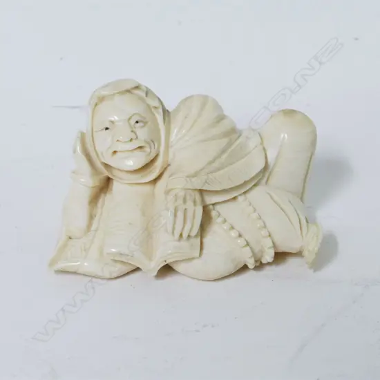 A carved ivory okimono of a reclining man reading a book